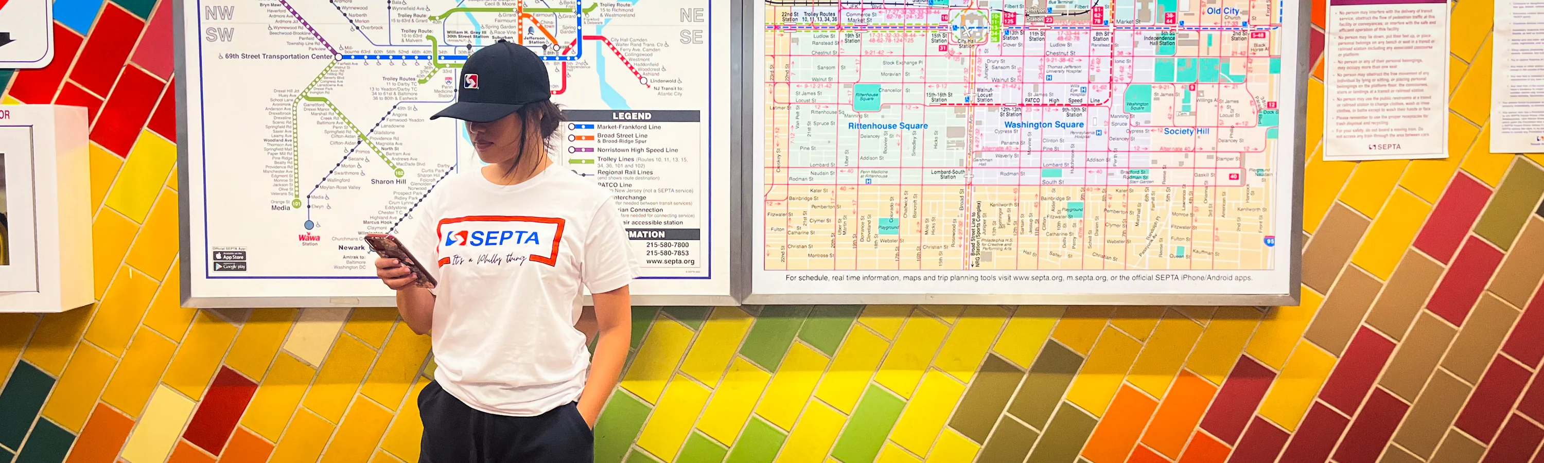 A model wearing SEPTA branded merch infront of a colorful tile wall and map